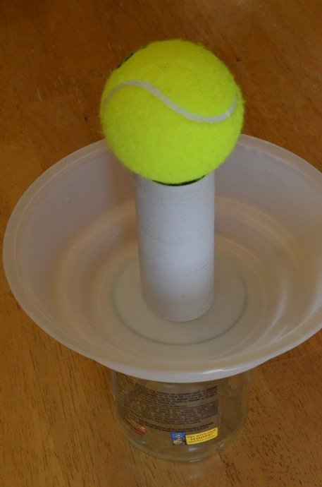 image of stacked glass, plastic bowl, toilet paper roll and the tennis ball