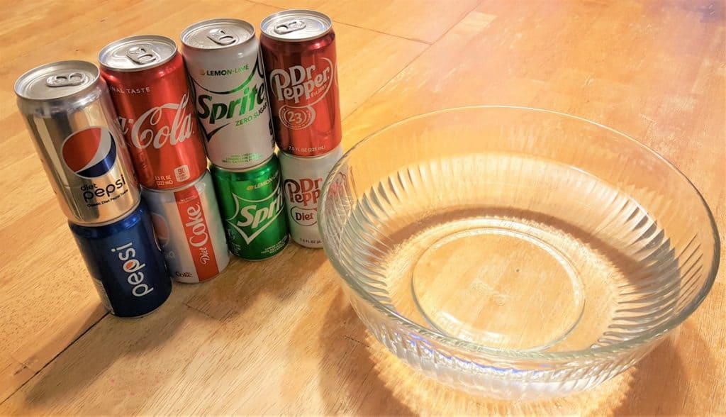 8 canned drinks stacked by pairs beside a large glass bowl filled with water